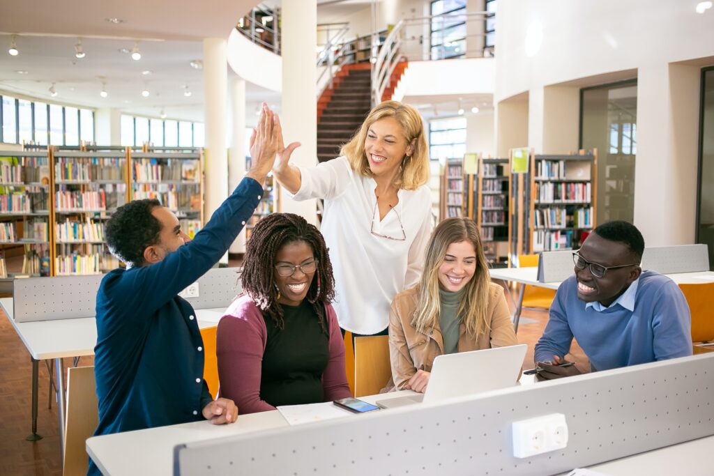 Diverse team in a library setting working together and giving each other a high five. Team has a sense of belonging.