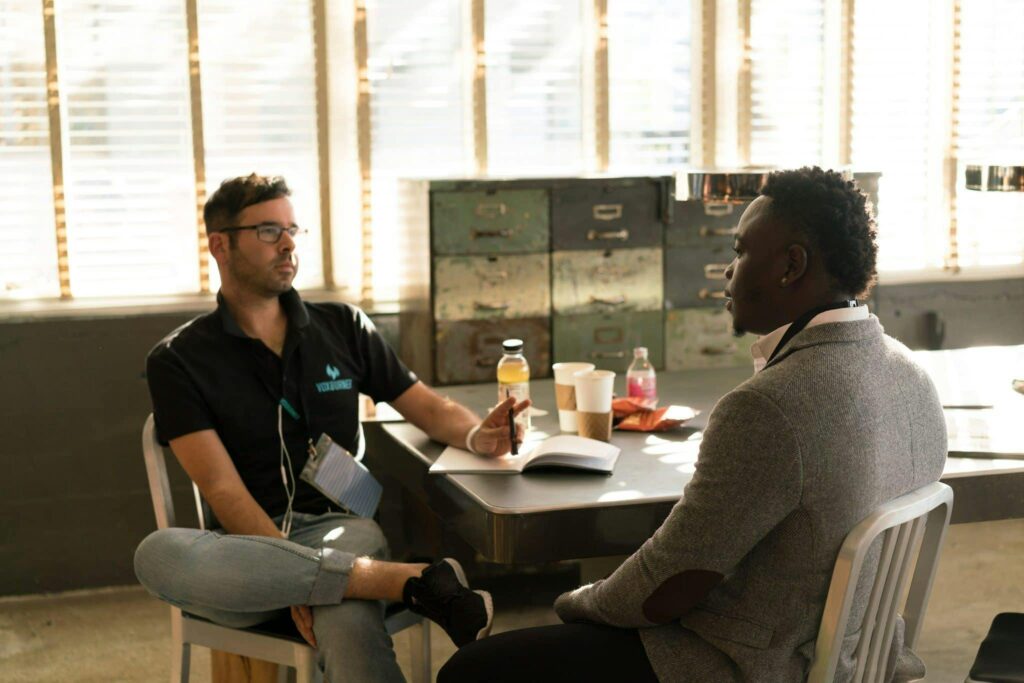 Two men sitting across from each other in a workplace setting, engaged in a professional conversation depicting a new employee meeting with their supervisor on the first day of work.